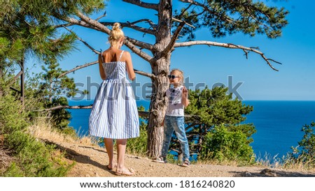 Mom and daughter on the sea near the cliff overlooking the blue sky are photographed in summer in sunny weather in a striped dress