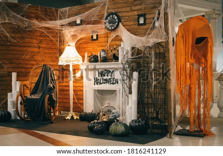 Photo area for Halloween with festive attributes. Fireplace, pumpkins, candles, skulls, bones, candles, chair, monsters decorations for Halloween indoors.