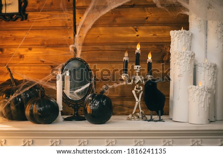 Close photo of Halloween scenery. Candles in candlesticks, black pumpkins in cobweb and crow on fireplace on wooden wall background, halloween decor concept