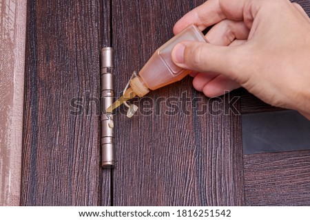 adjusting door hinge using lubricating oil. indoors. fixing door squealed domestic problem. Royalty-Free Stock Photo #1816251542