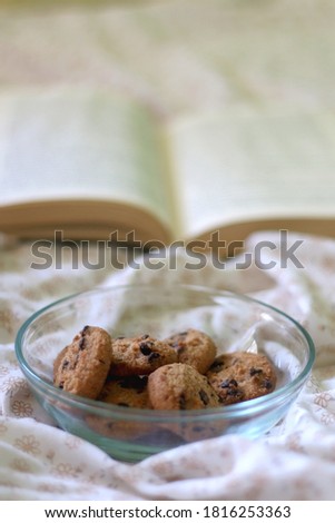 Bowl of chocolate chip cookies and open book on a bed. Selective focus.