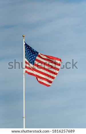 American flag blowing in the wind against a blue sky with wispy white clouds
