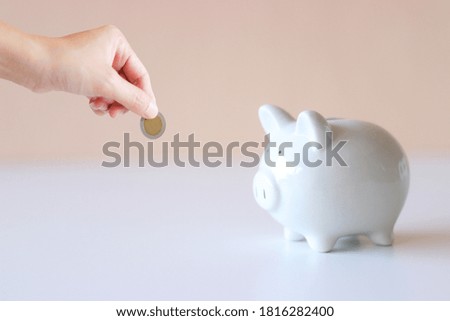 Saving piggy bank white pig on the floor It has a light pink background and a hand in charge of coin. Convey to savings