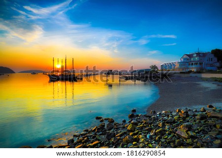 Morning sunrise at the Bar Harbor Inn in Maine with a large Sailboat highlighted by the raising sun.  Royalty-Free Stock Photo #1816290854