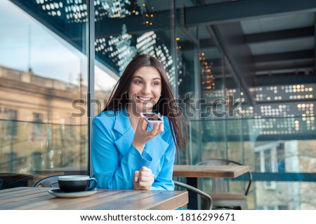 Portrait of a woman using the voice recognition of the phone sitting in a trendy cosy coffee shop cafe in Manhattan New York or at the balcony of her home