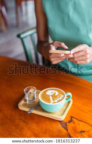 Close shot of woman hands holding mobile phone take photo of cup of coffee foam art in cafe.