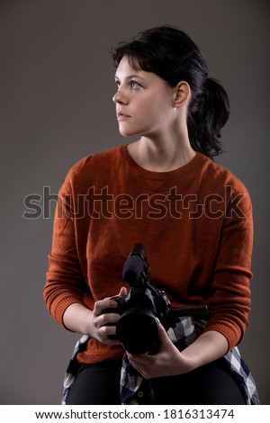 Portrait of a female online content creator holding a video camera used for vlogging.  She is an amateur filmmaker or an art student