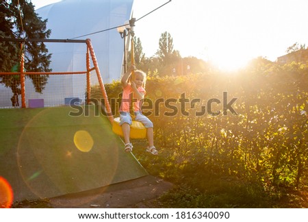 A little girl on a children's playground riding a trolley on a swing, special lighting, a child's silhouette, sun glare.