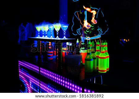 Professional barman and led light fire show. Silhouette of modern bartender shaking drink at night cocktail bar. 