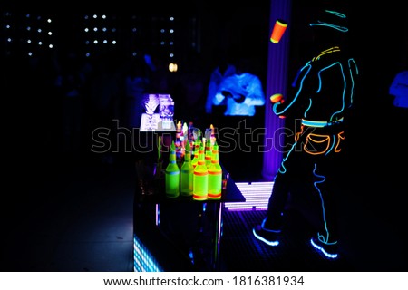Professional barman and led light show. Silhouette of modern bartender shaking drink at night cocktail bar. 