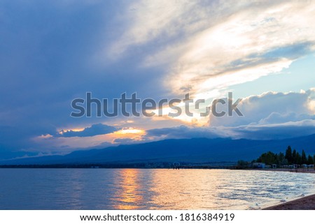 Beautiful sunset by the lake. Bright clouds are reflected in the water. A wonderful summer evening in nature. Kyrgyzstan.