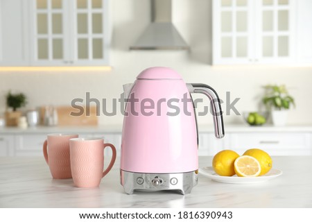 Modern electric kettle, cups and lemons on table in kitchen