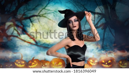 Witch surrounded by spooky pumpkins in misty forest on full moon night. Halloween fantasy