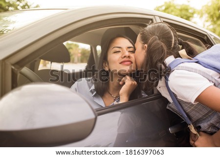 School girl kisses her mother before entering class. Young mother in the car, leaving her daughter at school.