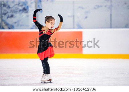 little girl figure skater in a light pink tracksuit with a smile skates on the ice on an indoor skating rink.