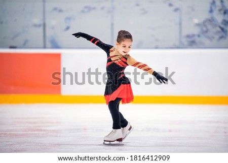 Little girl ice skater in a beautiful black red dress ice skating of an indoor ice arena.