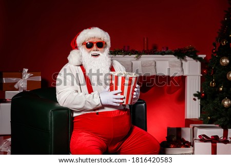 Photo of grey bearded santa claus sit in chair hold pop corn box with x-mas evergreen tree magic decoration isolated bright shine color background