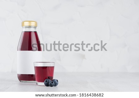 Fresh violet blueberry juice in glass bottle with blank label template with  glass, berries on wood table and white background with copy space.