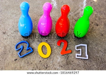 multicolored numbers of new year 2021 on cement background with kids bowling pins