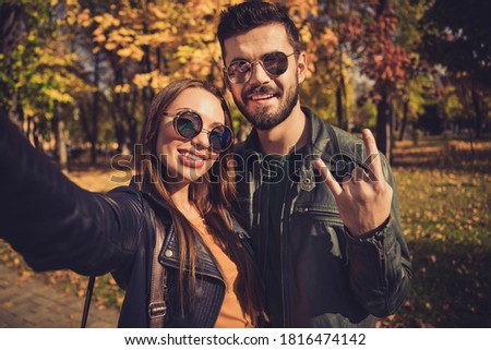 Photo of positive swag two people students couple make selfie show horned symbol in autumn city urban park wear jacket sunglass