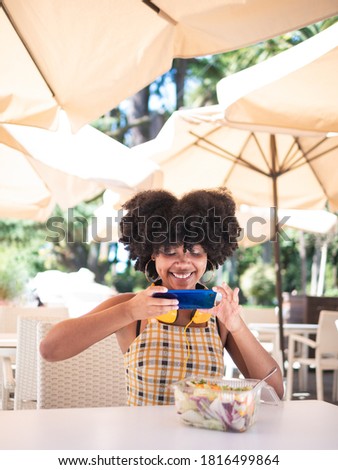 Young black woman sat on a terrace and taking a photo to a green salad, healthy food concept