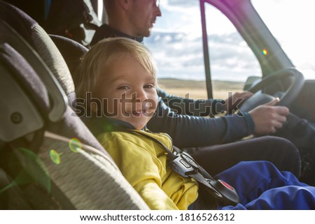 Cute toddler boy, kid sitting on the front seat in child seat on big camper van, smiling happily