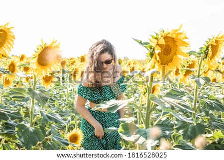 young woman dressed in green and with red sunglasses pictured among sunflowers in Guadalajara, Spain
