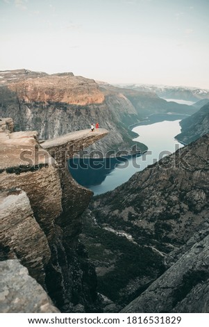 A man stands on his knee near the cliff and makes a creative proposal to a woman traveling in trolltunga, Norway. Emotional couple in love, engagement, rocks, nature, fjords. She said yes on the top. Royalty-Free Stock Photo #1816531829