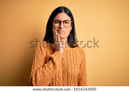 Young beautiful hispanic woman wearing glasses over yellow isolated background touching mouth with hand with painful expression because of toothache or dental illness on teeth. Dentist