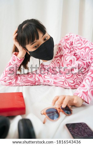 Young asian woman in pink shirt wear mask laying on bed with bored expression.