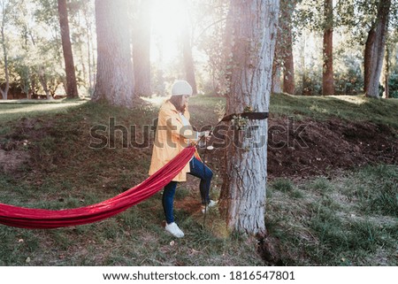 young woman wearing yellow raincoat preparing hammock to relax. Camping outdoors. autumn season