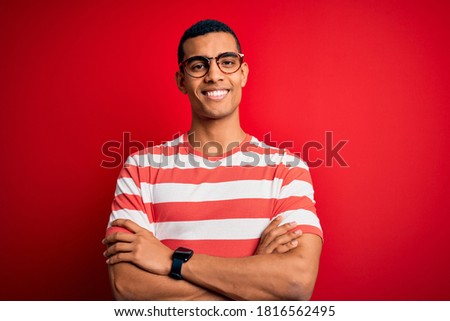 Young handsome african american man wearing casual striped t-shirt and glasses happy face smiling with crossed arms looking at the camera. Positive person.
