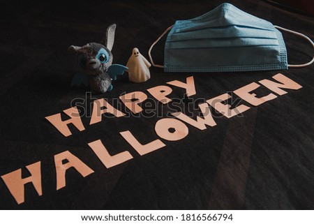 The words Happy Halloween written on a black background with a bat, a ghost and a covid-19 mask