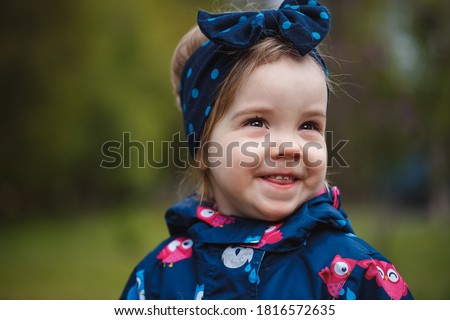 A little girl stands near a lush bush of lilacs, she smiles and sniffs purple flowers