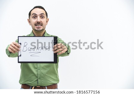 Brunette bearded man holding paper holder with word business writen on it, looking with comical face expression.