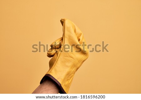 Hand of caucasian young man with gardener glove over isolated yellow background holding blank space with thumb finger, business and advertising