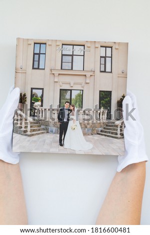 hands in white gloves holding a photo book with wedding photos. beautiful and convenient storage of the memory of an important day. Russian names Artyom and Arina are written on the cover.