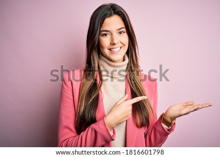 Young beautiful businesswoman wearing casual turtleneck sweater and jacket amazed and smiling to the camera while presenting with hand and pointing with finger.