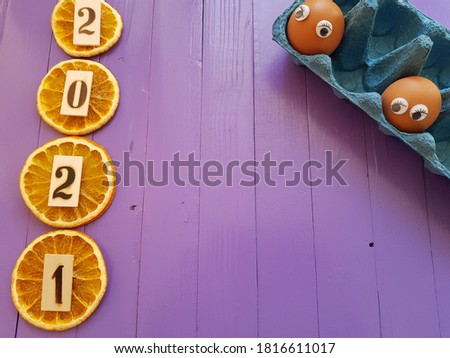 The year 2021 is written on orange slices. Nearby on a tray are chicken eggs with toy eyes