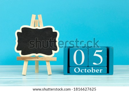 wooden calendar with the date of October 5 and an easel on a blue background, place for text, World Architect Day; World Teachers' Day; International Doctor's Day; International Day of Housing