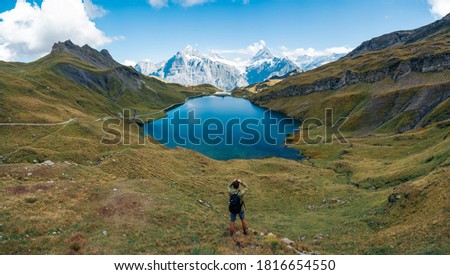 Enjoy the amazing view from top of the world. Hiker watching reflection of mountains at Bachalpsee lake, Switzerland. Panoramic banner of hiker on adventure trek. 