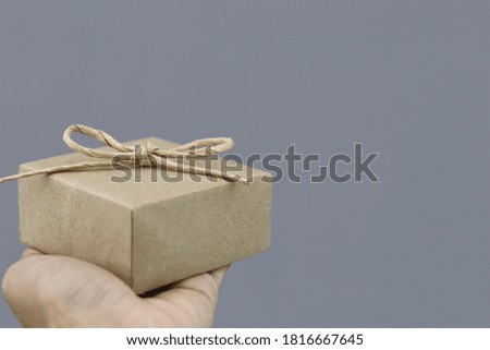 Close up shot of female hand holding gift box with gray background. Giving gift 