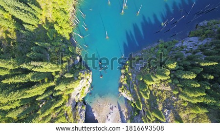 Coniferous trees rise from the depths of a mountain lake. Top view from the drone. On the shore you can see rocks, green forest and grass growing. Kaindy Lake, Kazakhstan. Groups tourists are resting. Royalty-Free Stock Photo #1816693508