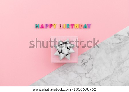 Happy birthday inscription from wooden colorful letters with gift box. Birthday poster template on pink and marble background