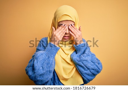 Young beautiful brunette muslim woman wearing arab hijab over isolated yellow background rubbing eyes for fatigue and headache, sleepy and tired expression. Vision problem