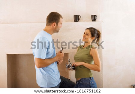 Happy couple doing DIY at home standing beside fireplace holding new faucets and talking.