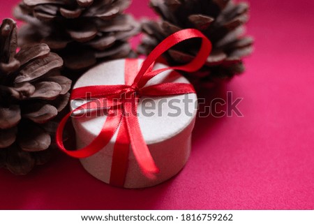 Christmas gift from a round box, tied with a red ribbon on a red background with wooden cones. The view from the top. Space for text. A soft picture.