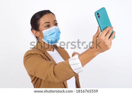 Portrait of a pretty happy businesswoman wearing medical mask taking a selfie isolated over bright background