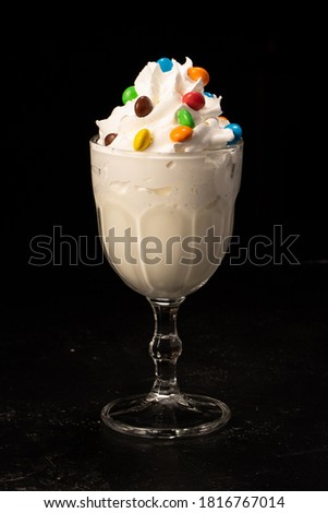 Classic milkshake decorated with sweets and whipped cream in a transparent glass on a black background