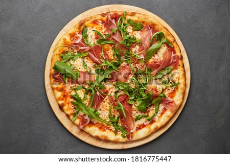 Delicious Italian Pizza with Parma ham and arugula, mozzarella cheese on dark background